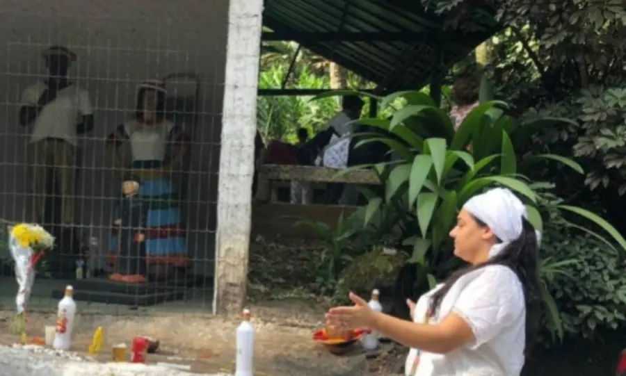 Yalorixá Cigana de torço branco abrindo as mãos diante de uma oferenda com velas e flores